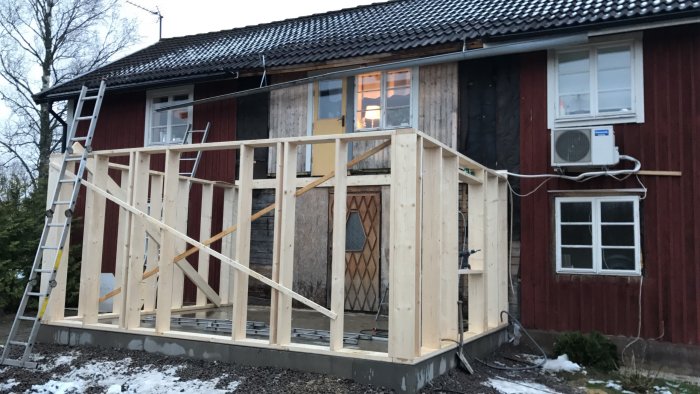 Tillbyggnad under konstruktion på ett rött hus med snöfläckar på marken.