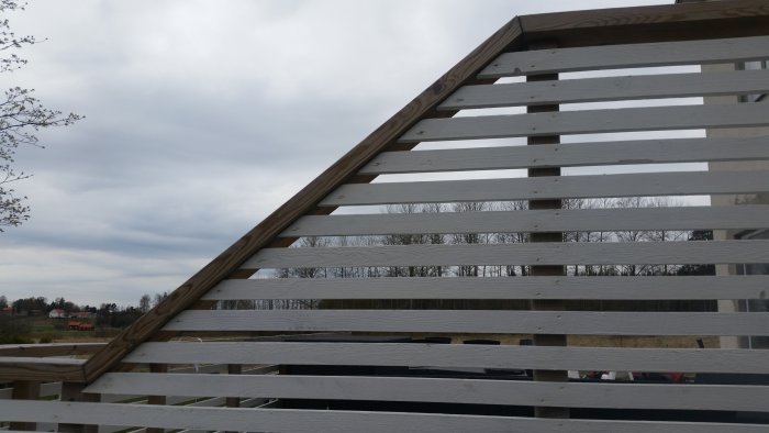 Skråade träplank i ett staket med öppen landskapsvy i bakgrunden.