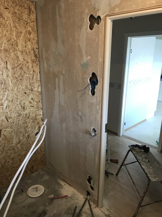 Renoveringsarbete med eldragning, synliga sladdar och hål i vägg för installationer, osb-vägg och arbetsmaterial.