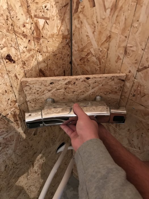 Hand som installerar en termostat på en OSB-panelvägg under en badrumsrenovering.