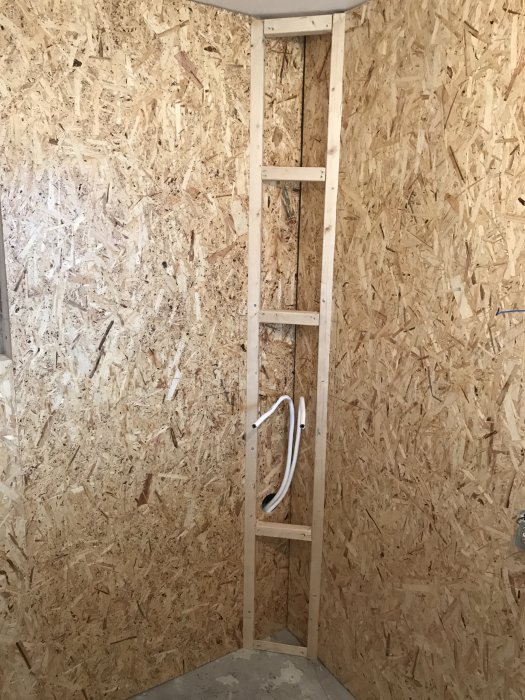 OSB-väggar med träreglar och genomförda kablar i en hörnkonstruktion under en renovering.