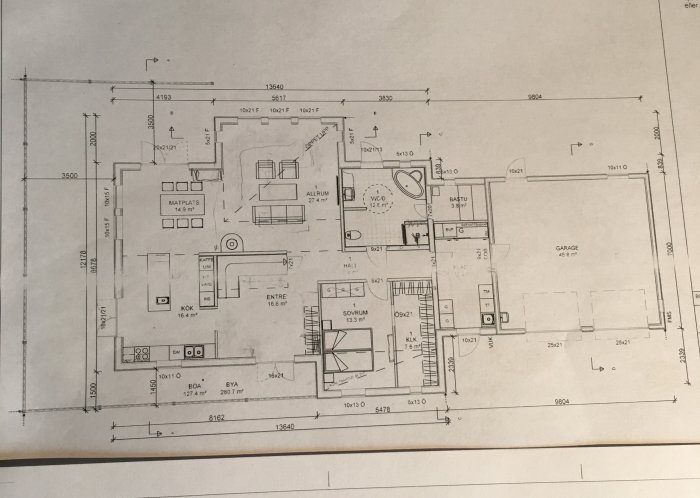 Arkitektritning av enplanshus inkluderar kök, vardagsrum, garage, och dimensioner; möbler sugerierade schematiskt.