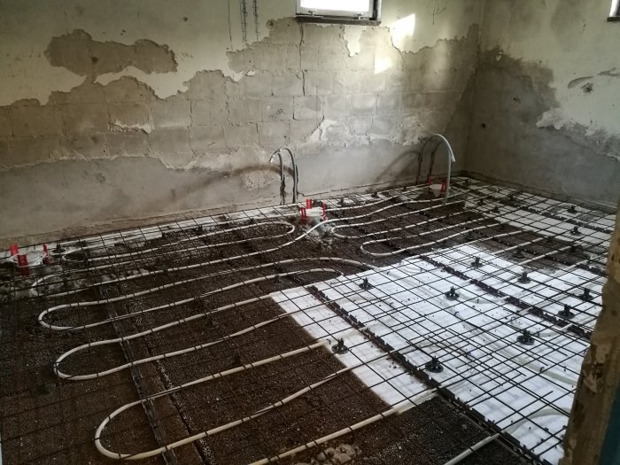 Renoverat rum med nygjuten betongplatta, armeringsnät och golvvärmerör på golvet mot råa betongväggar.
