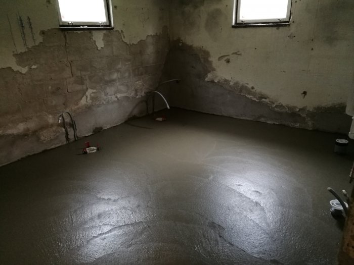 Nyggjutet betonggolv med fall mot golvbrunnar i ett rum med betongväggar och fönster.