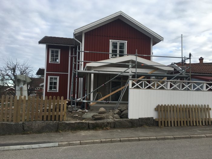 Rödmålat hus med byggnadsställningar och tillbyggnad under konstruktion.