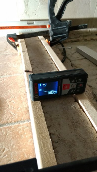 Digitalt vattenpass visar 0,00 cm på en trälist mot en putsad vägg under en byggrenovering.