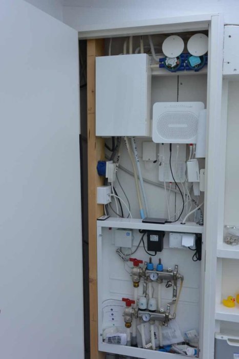 Elcentral med öppen kapsling som visar golvvärmestyrning, fiberanslutning och dimmer doser.