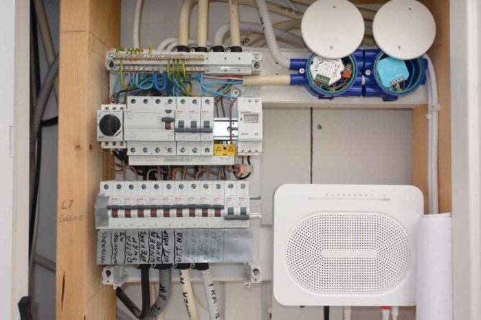 Elektriskt apparatskåp med öppen kapsling visar elcentral, fiberanslutning, router och dimmers i en heminstallation.