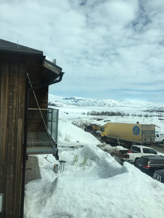 Snöig utsikt vid riksgränsen med hus, balkong och lastbil på parkering.