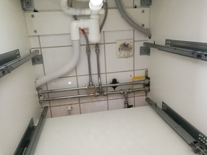 Installeringsplats under handfat med rörledningar, eluttag och plats för tvättmaskin.