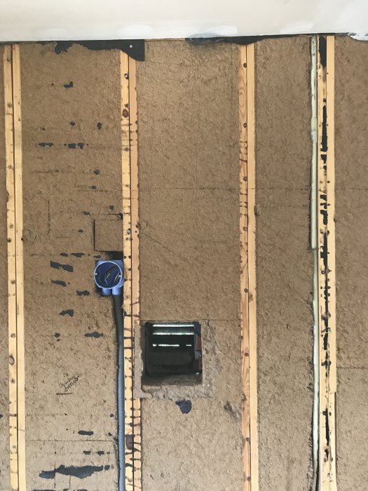 Isolerad vägg under renovering med ett igensatt hål och synliga träreglar samt en måttband till vänster.