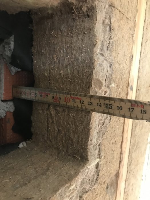Mätning av ett igensatt hål i en fasad inifrån ett hus, med synlig isolering och en del av ett måttband som visar centimeter.