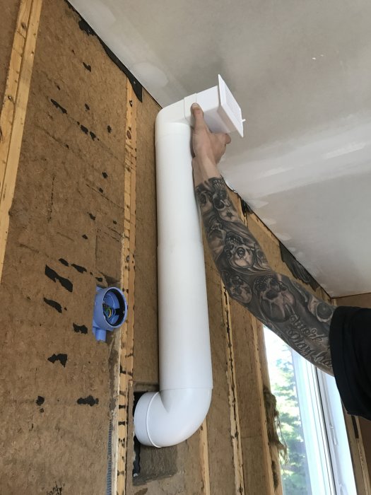 Vit ventilationsrör som leder till ett hål i väggen under köksrenovering, nära ett fönster.