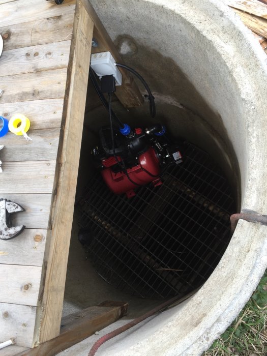 Vattenpump och anslutningar i en betongbrunn för trädgårdsbevattning.