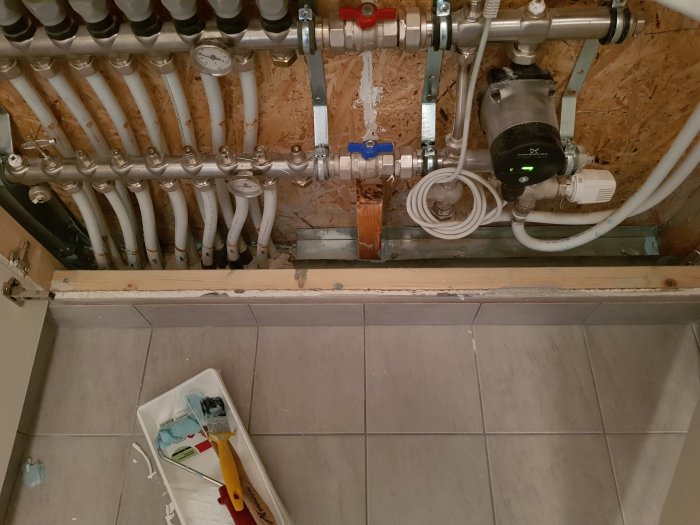 Renoverat väggutrymme med golvvärmerör, pump och åtgärdade läckagepunkter, ovanpå grå klinkergolv.