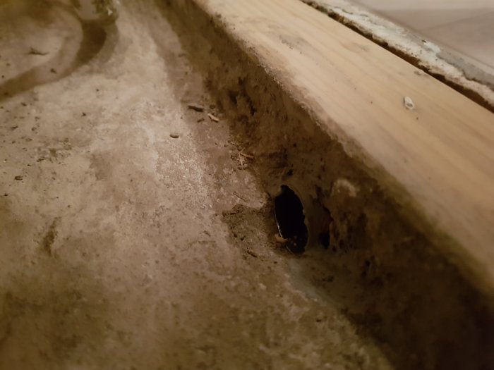 Bild av ett hörn med betonggolv och trävägg, inklusive ett rörmyntningshål för golvvärme.