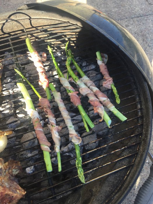Sparris lindade i bacon som grillas på en kolgrill.