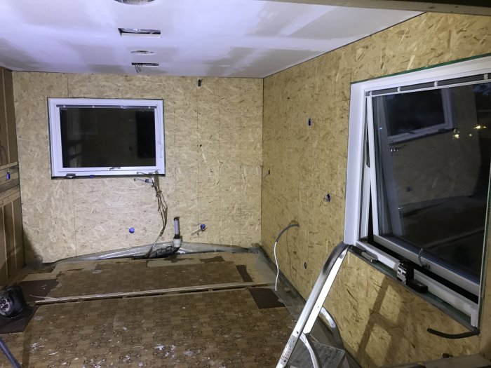 Under renovering rum med OSB-väggar, två fönster och elinstallationer synliga.