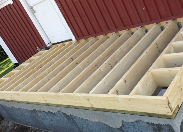 Nyligen färdigställt träbjälklag vid husbygge, med exponerade träbjälkar på betonggrund.