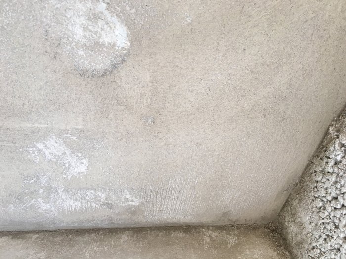 Putsad vägg med synliga sprickor och ränder, kritvit fläck i övre vänstra hörnet.
