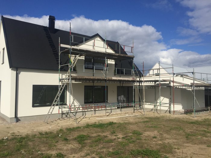 Nybyggt hus med ställningar runtom, plats där altan med pergola planeras att byggas.