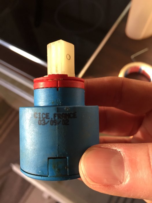 Hand håller upp en blå och röd elektrisk anslutningsterminal mot en suddig bakgrund.