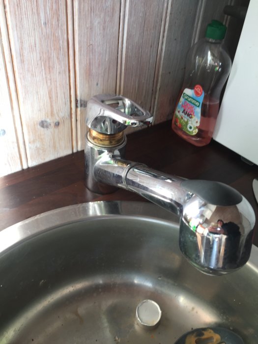 Kökskran över diskho med diskmedelsflaska och träskåpsluckor i bakgrunden.