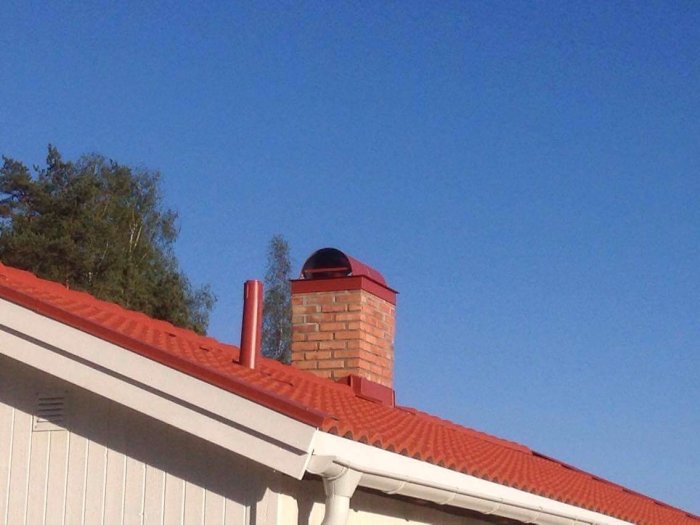 Nyrenoverad skorsten med huv och rött tegeltak på ett hus, mot en klarblå himmel.