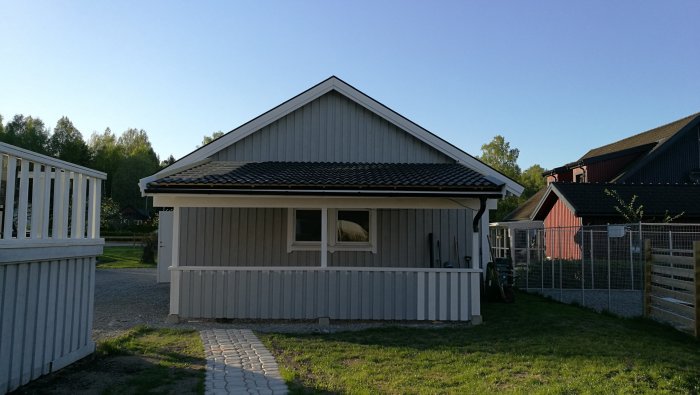 Nybyggd carport med grå panel och svart tak, intill ett enfamiljshus på en solig dag.