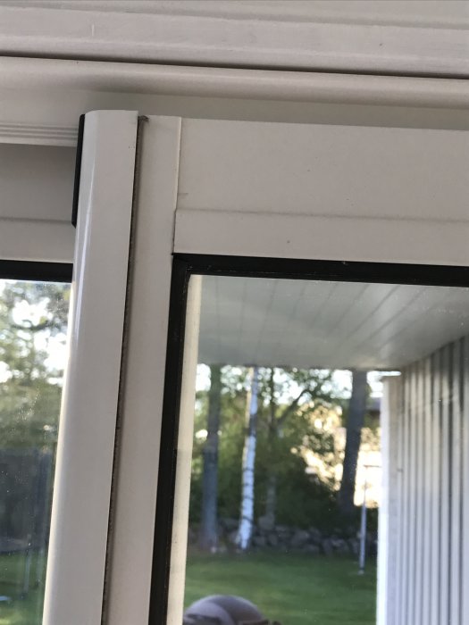 Utsnitt av en dörr i ett uterum där ramen inte sluter tätt mot listerna, med utsikt till en trädgård.