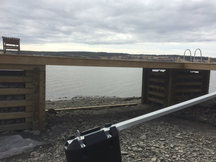 En planka på marken vid en havskant med en delvis synlig träkonstruktion och himmel i bakgrunden.