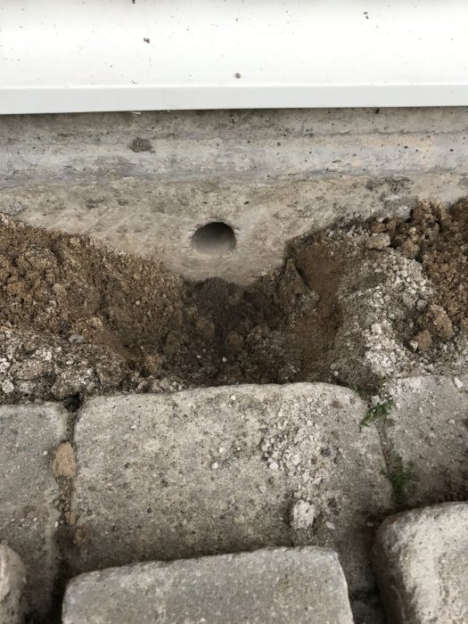 Golfboll-stort hål i husgrund under borttagna plattor, omgivet av sand och grus.