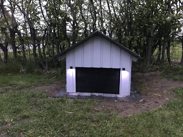 Hus för Gardena R50 med öppen port och RGB LED-belysning i skymningen, placerat på gräsmatta.