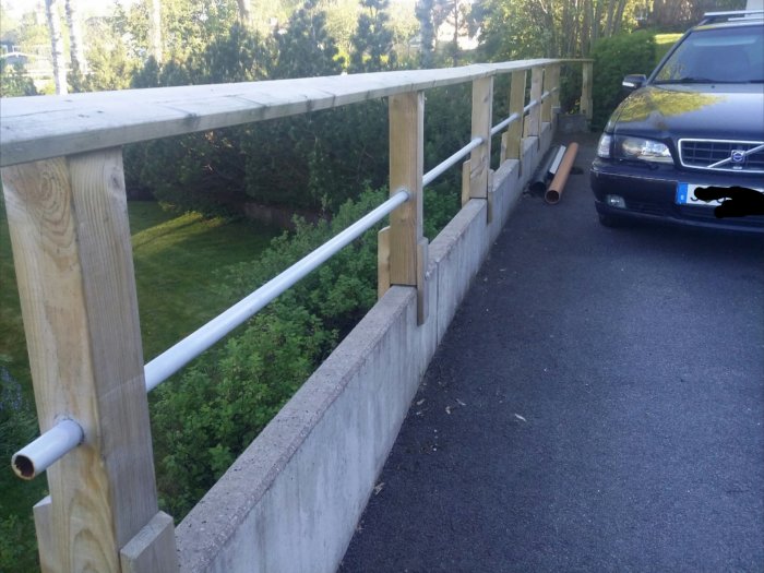 Gelænder lavet uden at bore i støttestruktur, træ og metal langs asfalteret indkørsel med bil parkeret.