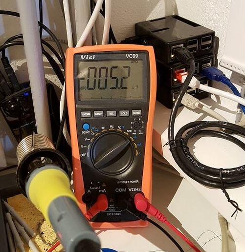 Multimeter som visar 0.52 på displayen, omgiven av elektroniska kablar och utrustning.