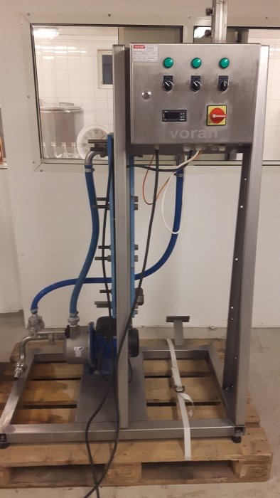 En pastöriseringsenhet på en träpall med sladdar och slangar anslutna.