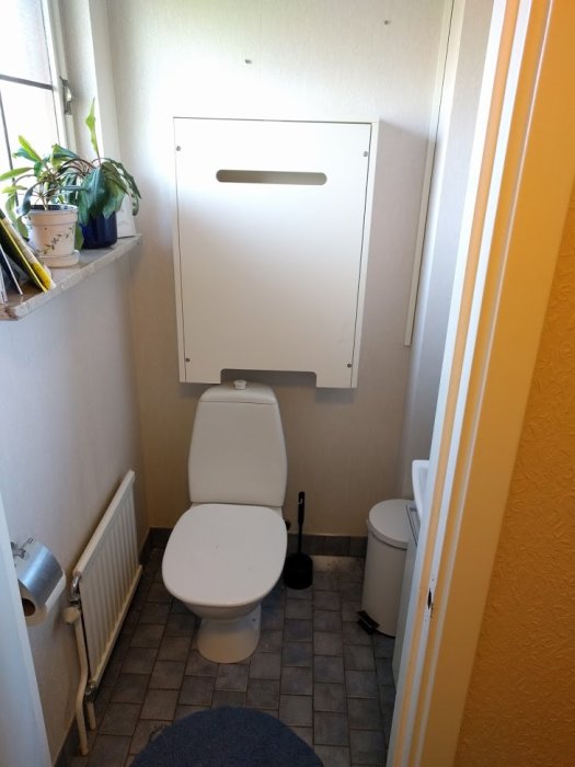 Skötbord anpassat och monterat ovanför toalettstol i litet badrum, rundad öppning i underkant synlig.