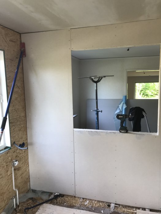 Inre väggbeklädnadsarbete med gipsskivor i ett rum under renovering, exponerade rör och isolering synliga.