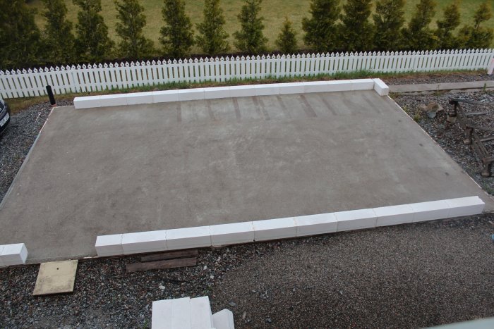Nygrundlagd platta med limmade lättbetongblock längs kanten på en grusig byggplats.
