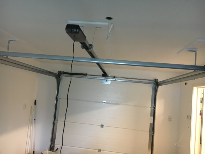 Nyinstallerad garageport med automatisk portöppnare och ledningar längs taket i ett nymålat garage.