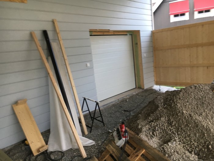 Nymålat hus med grå fasad, ny garageport och byggmaterial framför pågående uterumsbygge.