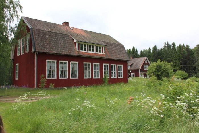 Rött trätorp från 1926 med vita fönster omgivet av grönskande natur.