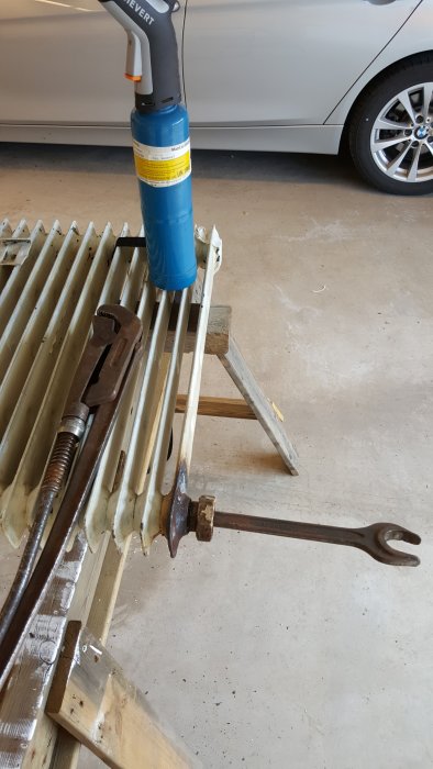 En värmepistol riktad mot en radiator med en rörtång och anpassad nyckel redo för reparation.