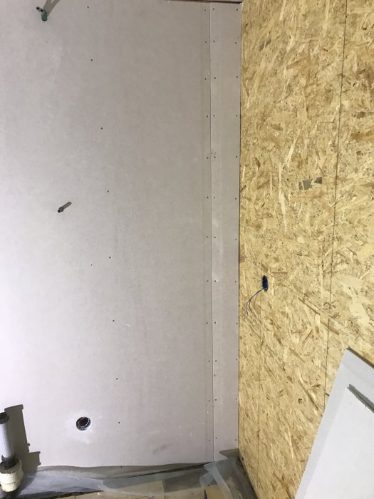 Vägg under renovering med spacklade skruvhål och osminkade OSB-skivor.