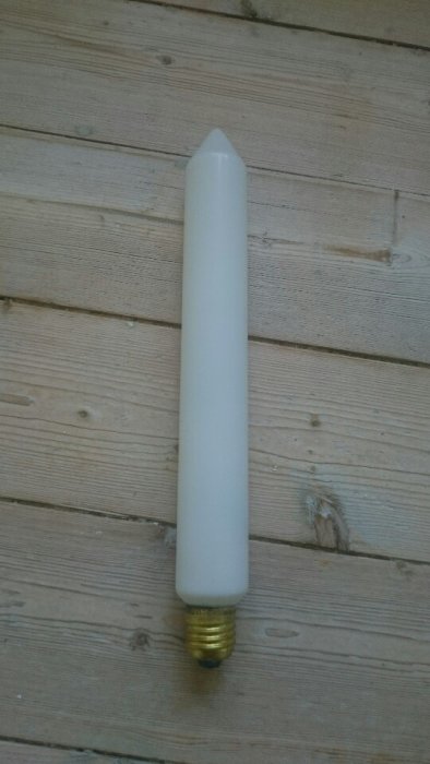 Glödlampa av lång, smal typ med E27-sockel mot träbakgrund.