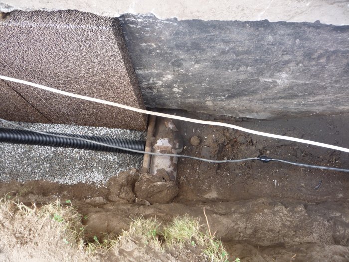 Grund av byggnad med isolering och rör synliga i grävd dräneringsdike.