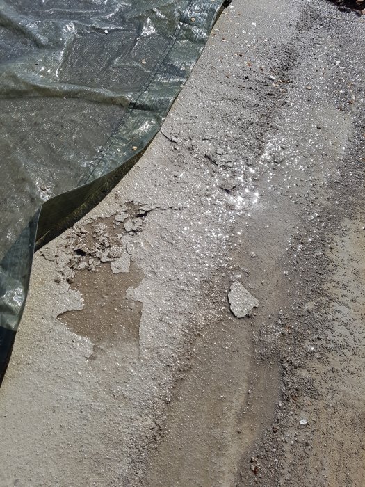 Nyligen gjuten betongyta på altan med tunn hinna som lossnar, delvis täckt av presenning.