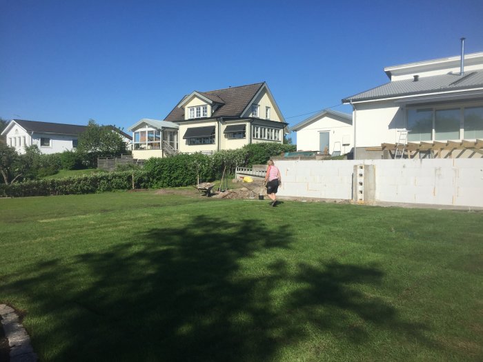 Nyutlagt gräs framför hus med pågående bygge av pooldäck och person som vandrar.