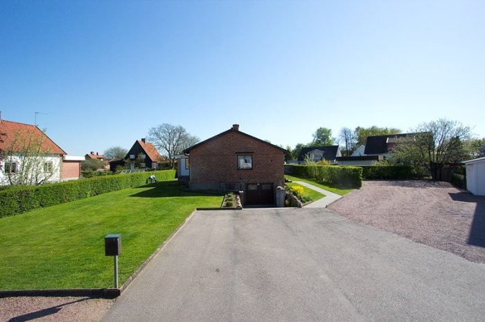 Enfamiljshus med tegelfasad och gräsmatta under en klarblå himmel.