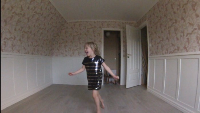 Glatt barn springer i ett nyligen renoverat rum med tapetserade väggar och vit panel.